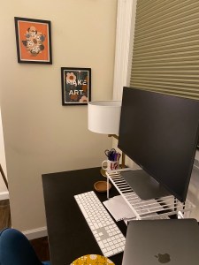 A desk with a monitor, laptop, and keyboard. Behind the desk are two framed art pieces, one reads "Make Art."